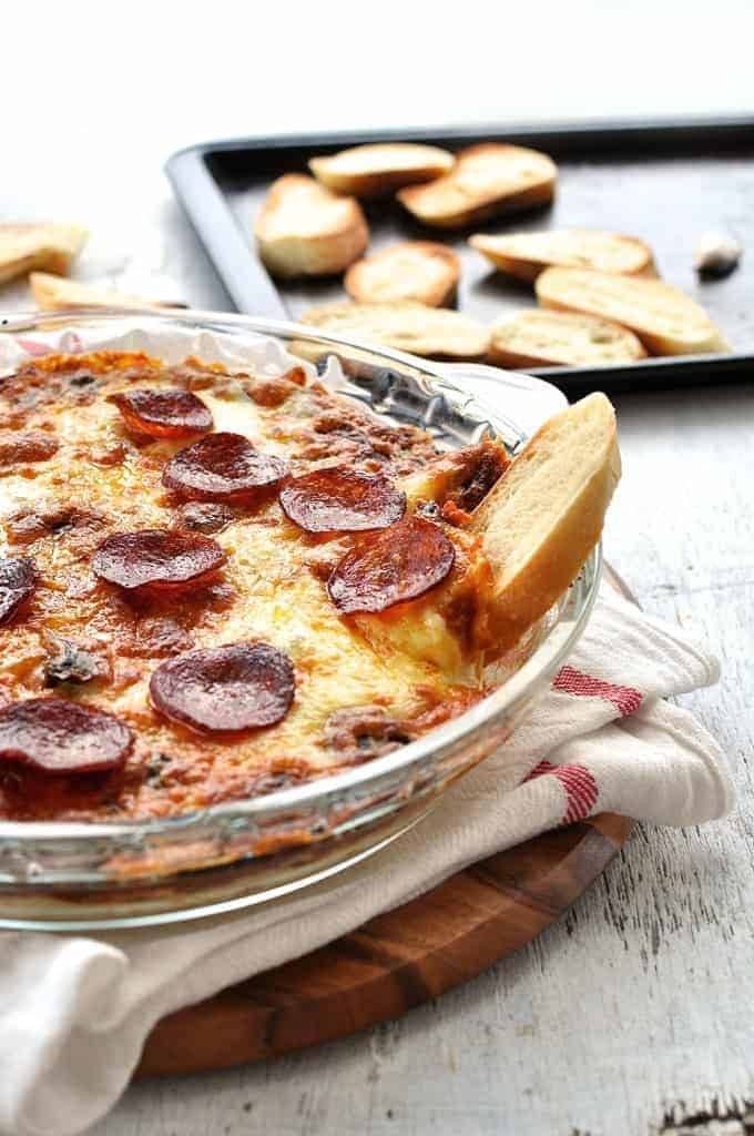 Toasted bread stuck on the side of an ultra cheesy, gooey Pizza Dip in a glass dish.