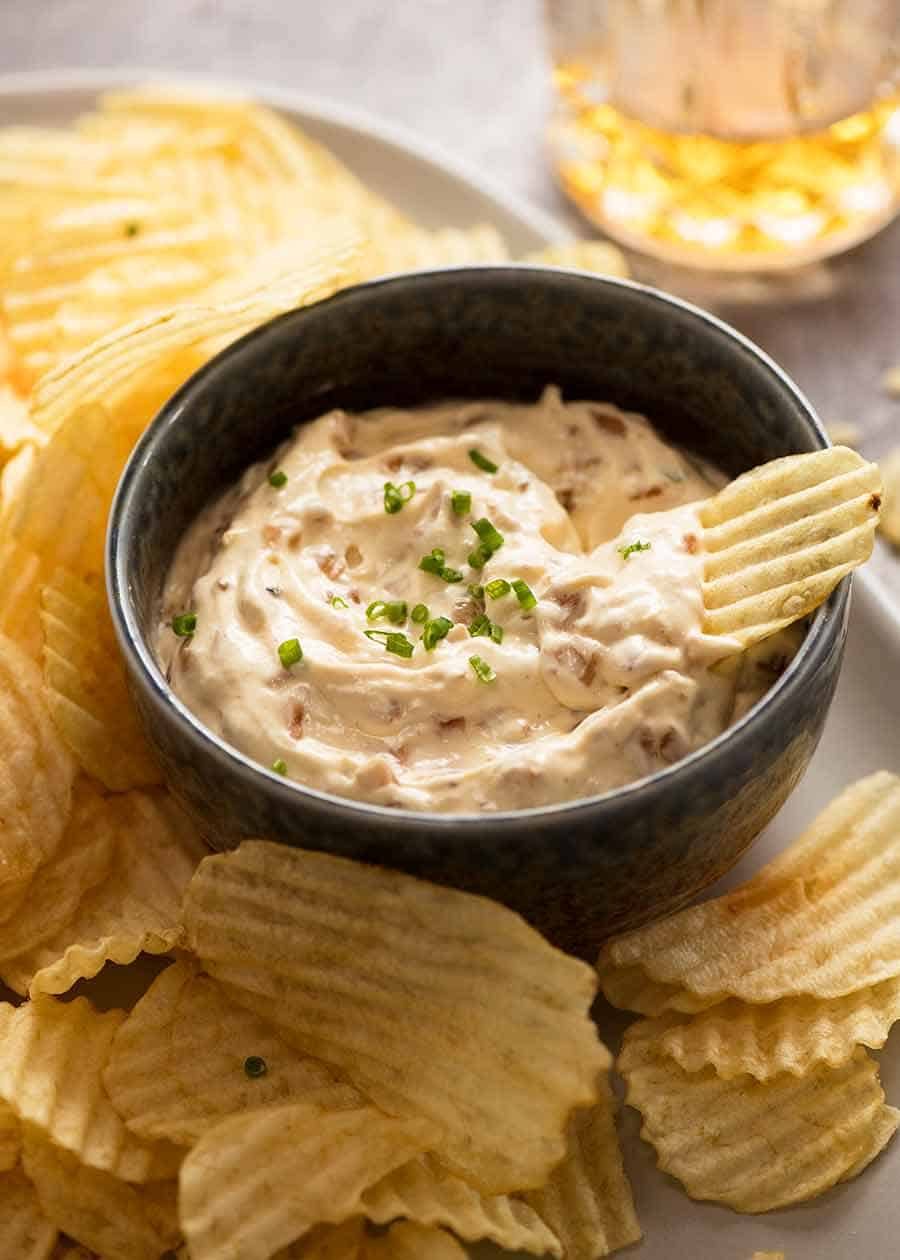 French Onion Dip in a blue dish surrounded by crinkle cut potato crisps, ready to be served at a party
