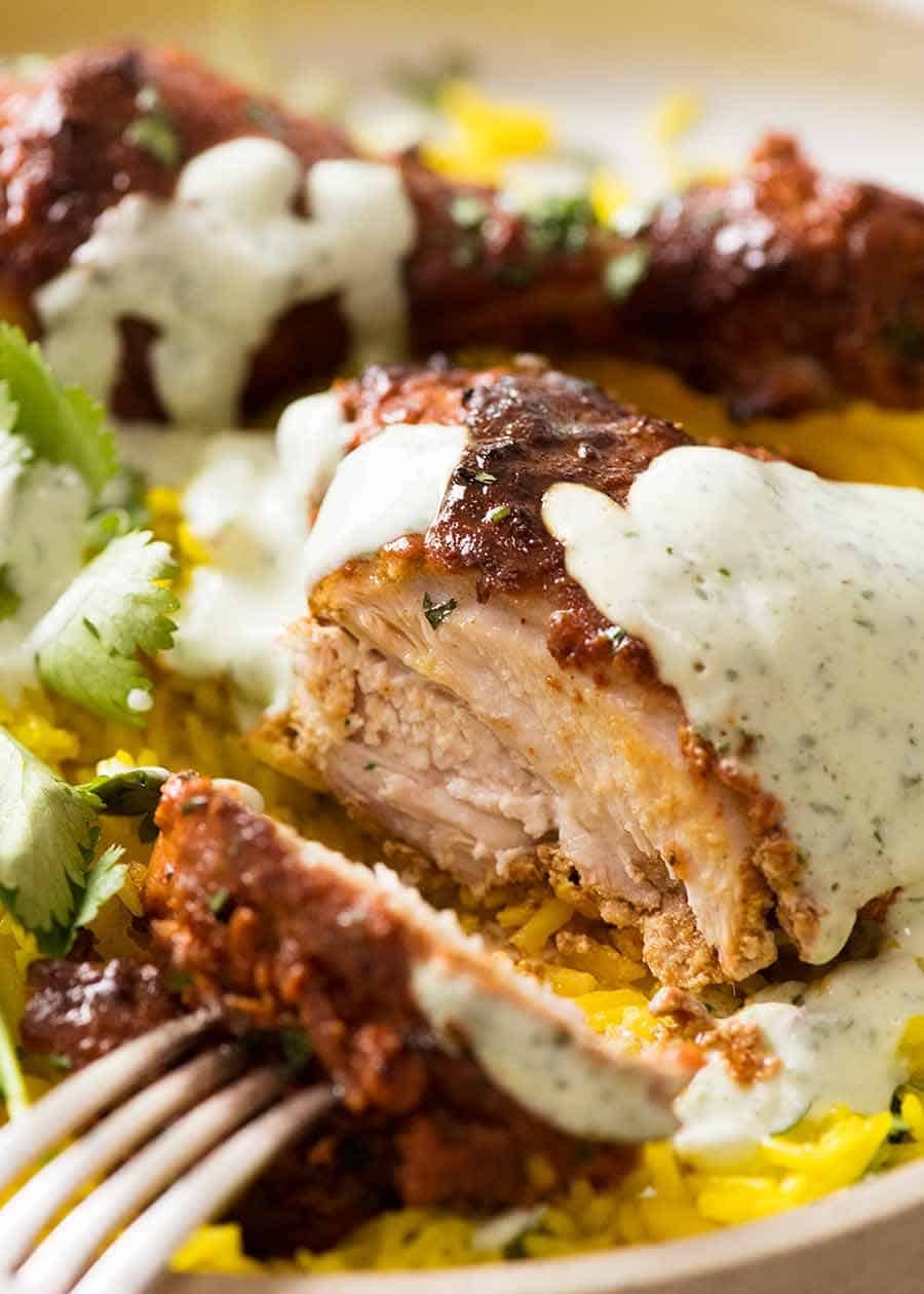 Close up photo showing juicy inside of tandoor chicken with saffron and minted yogurt sauce