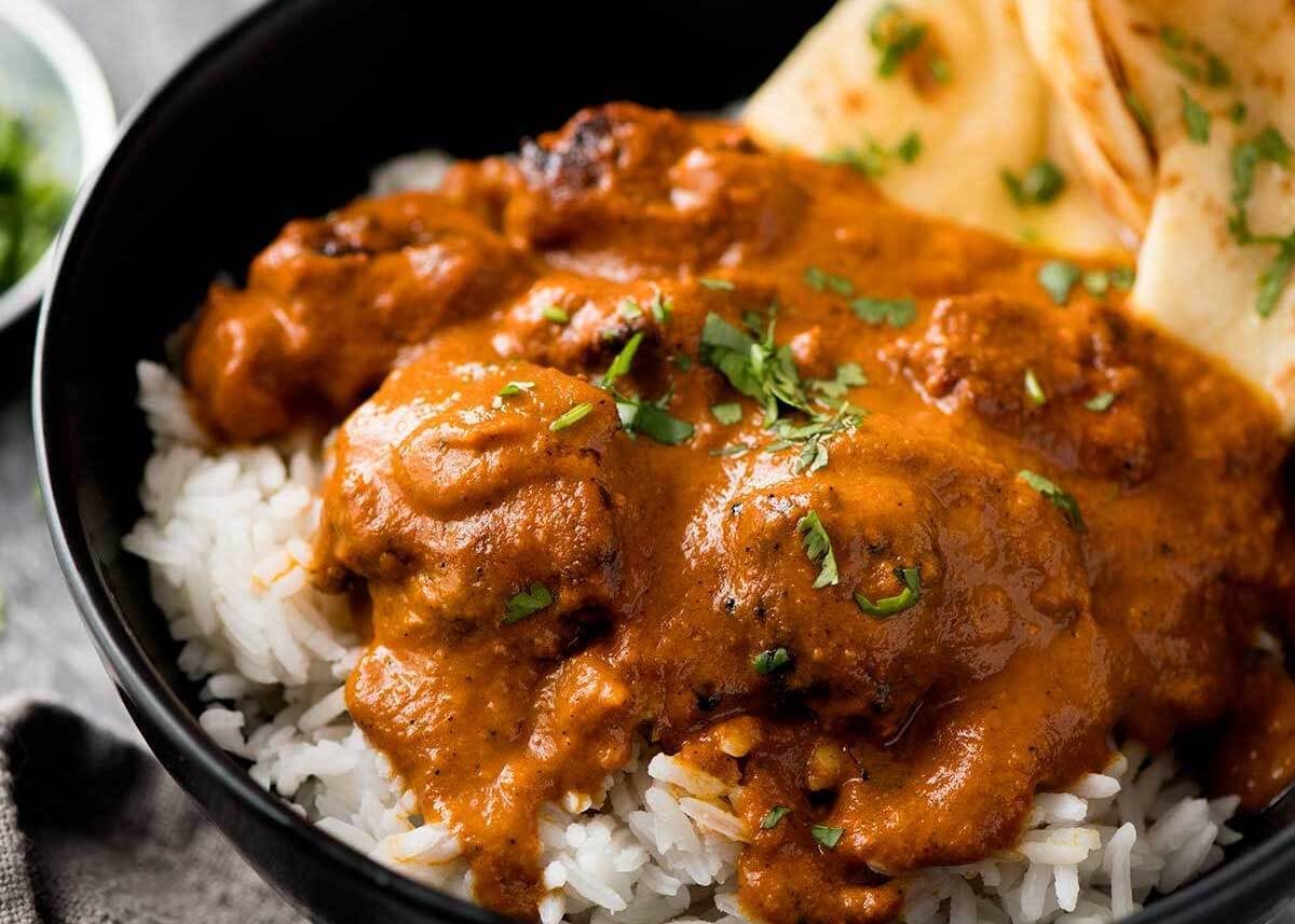 Close up of Chicken Tikka Masala over rice in a dark bowl, garnished with coriander / cilantro.