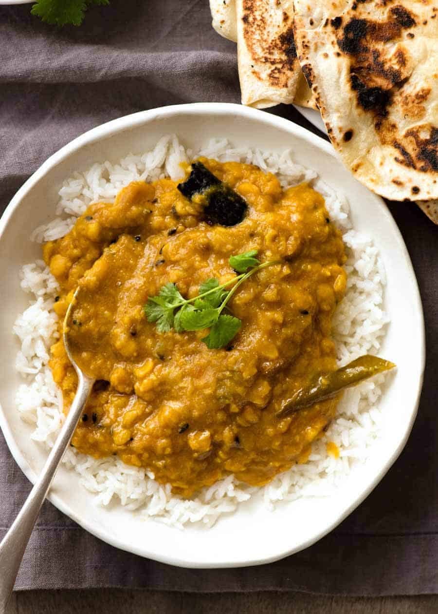 Overhead photo of homemade India lentil curry (Dal) served over rice in a rustic white bowl with a side of chapati, ready to be eaten.