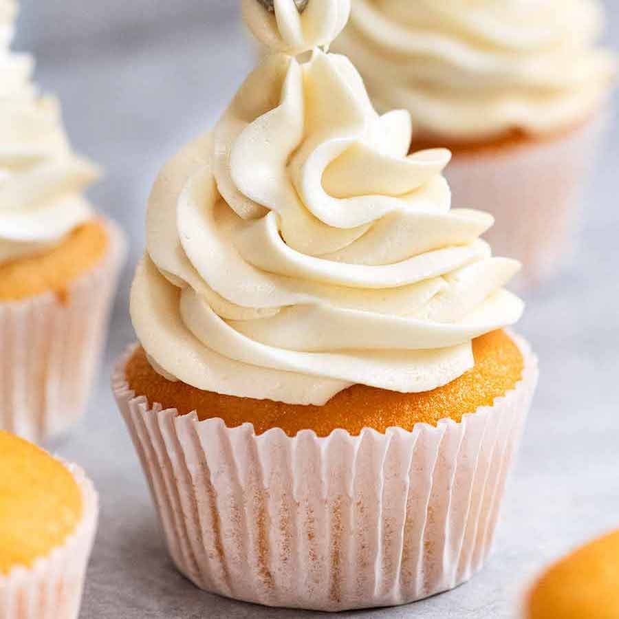Close up piping Fluffy Vanilla Frosting onto Vanilla Cupcake